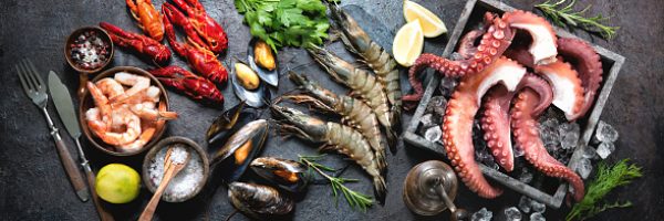 Variety of fresh delicious seafood. Octopus tentacles, black tiger shrimps, king prawn and mussels with fresh herbs and seasoning on black rustic background